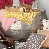 Close up image of boho style decor featuring a metal stool, pillows, and colorful fabric