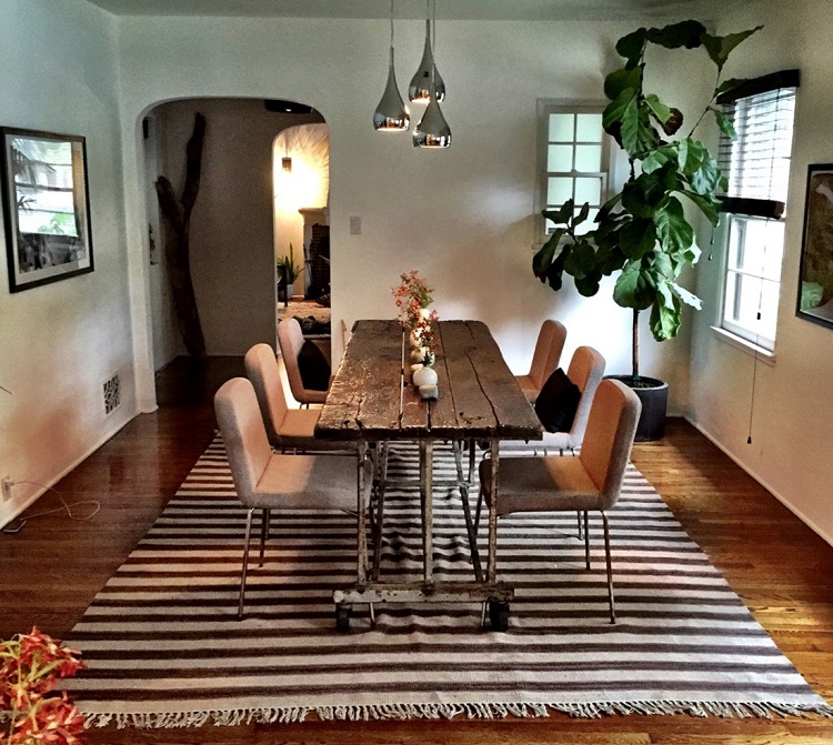 Dining room table with chairs over rug and beneath hanging pendants